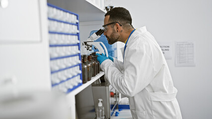 Hispanic man with beard working in laboratory analyzing samples through microscope
