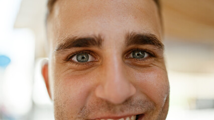 Close-up portrait of a cheerful young hispanic man on a sunny urban street, showcasing his engaging smile.