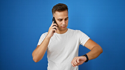 Handsome young man checking time while talking on smartphone against blue background.