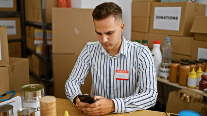 A young handsome man named alex using a smartphone in a warehouse with boxes and food donations...