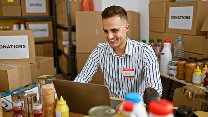 Handsome hispanic man named alex volunteering at a donation center, smiling while using a laptop.