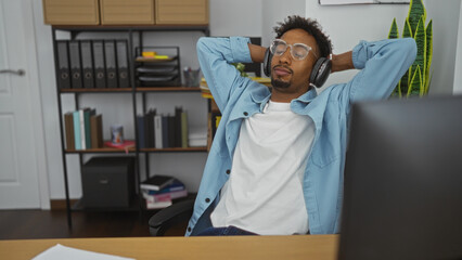 Young african american man relaxing with headphones in an office.