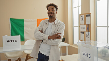 Young adult man with beard standing with arms crossed in an electoral college room with an irish...