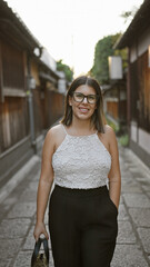 Confident hispanic woman, beautiful and joyful, cheerfully posing with glasses on, standing and smiling on kyoto's traditional streets, radiating natural and carefree latin expression.