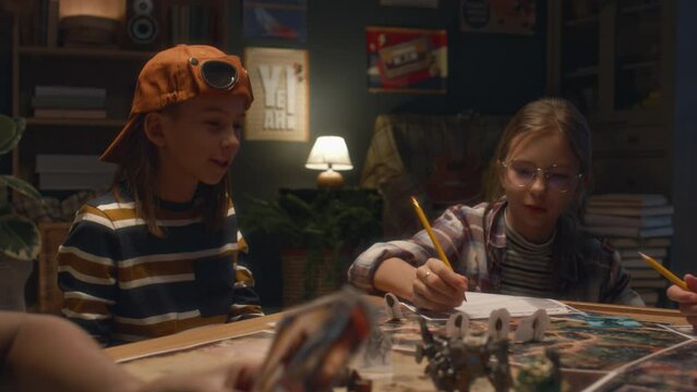 Handheld shot of diverse little friends gathered together in evening to play board game at home