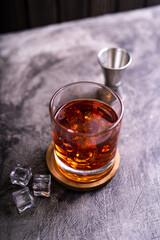 Whiskey, bourbon or cognac on glass with ice cube on a rustic wooden background with copy space
