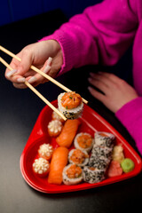 Assorted sets of sushi on a dark table in a hand of girl in a pink