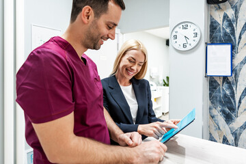 Obraz premium Beautiful and happy blonde woman at beauty medical clinic. She is talking with handsome doctor about face aesthetic treatment.