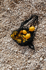 Mediterranean picnic: string shopping bag with lemons lying on the pebble beach with small white stones