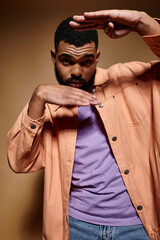 Handsome African American man posing in fashionable orange jacket and purple shirt against vibrant backdrop.