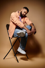 African American man in fashionable attire seated, legs crossed.