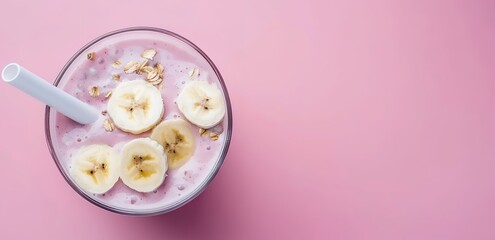 A glass of juice topped with banana photographed over a pink background
