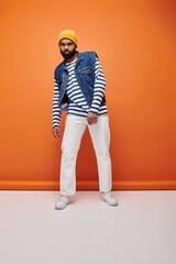 Handsome African American man posing in fashionable attire against a vibrant orange backdrop.