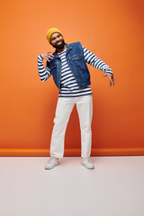 Handsome African American man in striped shirt and jean jacket posing on a vibrant backdrop.