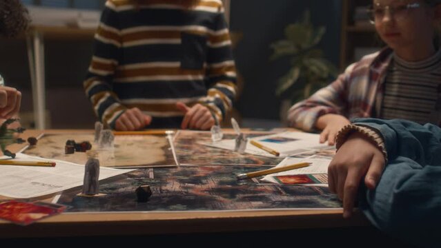 Tilt shot of boy rolling multi sided dice during his turn in tabletop game, playing with diverse friends at home in evening