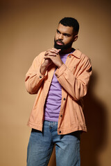 Fototapeta premium Fashionable African American man poses against a striking brown wall.