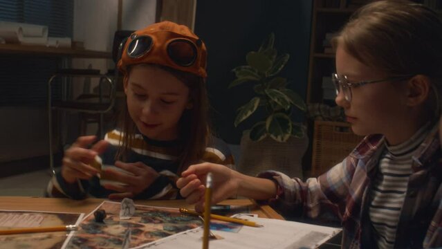 Side shot of little girl in glasses rolling polyhedral dice and boy telling number during board game in company at home in evening