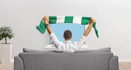Man sitting on a couch and cheering with a scarf