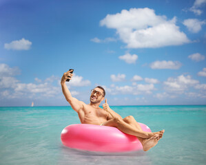 Man gesturing thumbs up, sitting on a swimming ring and taking a selfie with a smartphone