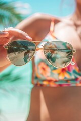 Naklejka premium Close-up of a hand holding a pair of vintage aviator sunglasses, revealing a faded floral swimsuit