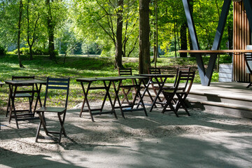 Empty wooden tables and chairs in a summer cafe in a green park