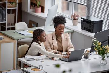 Wide angle shot of multiethnic business women discussing new design project while working together on laptop in corporate office © Seventyfour