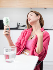 Tired and overheated attractive woman suffering from a heat attack uses an electric handy fan to...