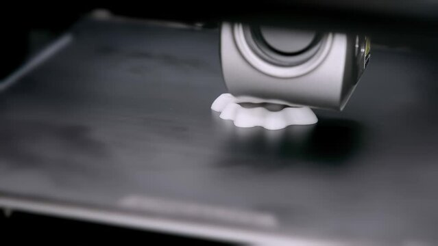 A portal with a carriage and a print head of a 3D printer that prints with white plastic on a printing platform. additive manufacturing concept