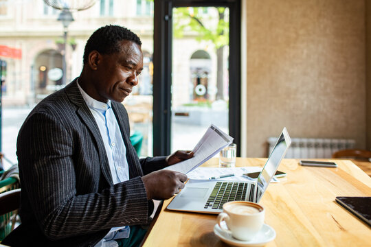 Mature businessman reviewing documents while working on laptop in a cafe