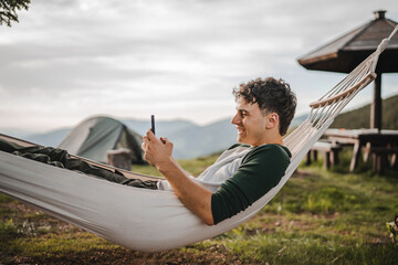 Young boy lying down in hammock and use mobile phone on the mountain