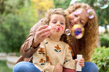 Mother and daughter are blowing bubbles in a park