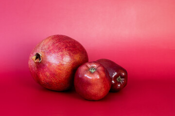 Ripe pomegranate and red apples on a red background with copy space