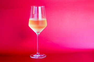 White wine in a glass on a red background with copy space.