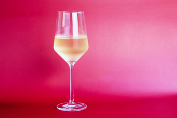 White wine in a glass on a pink background, close-up