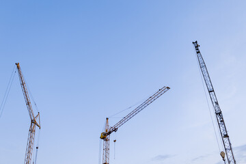 Construction site. Many tower cranes on dusk blue sky background. Construction multi-storey residential and commercial real estate. Industry new building business. Mortgage concept