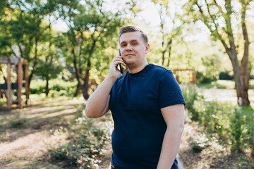 Obraz premium Happy blonde 30s man talking on smartphone in city park. Communication and gadgets, connection concept