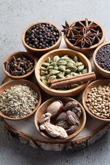 Set of various whole warming Indian spices in wooden bowls on a gray background vertical