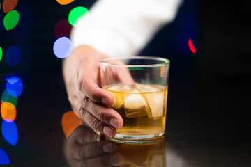 Closeup of professional bartender serving a cocktail in the glass with one big ice cube on the bar counter in the blurred background