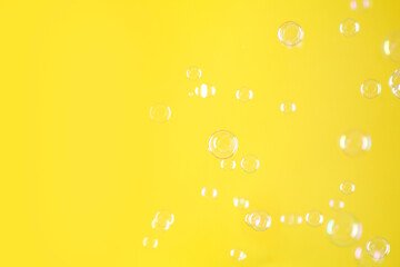 Beautiful transparent soap bubbles on yellow background, space for text