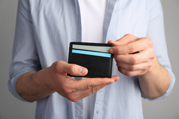 Man holding leather business card holder with cards on grey background, closeup