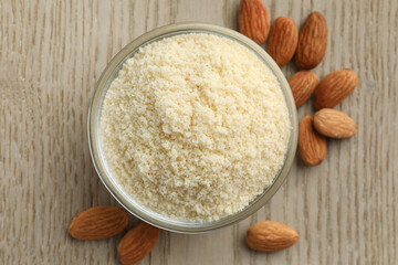 Fresh almond flour in bowl and nuts on wooden table, top view