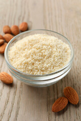 Fresh almond flour in bowl and nuts on wooden table, closeup