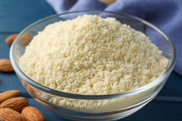 Fresh almond flour in bowl and nuts on blue wooden table, closeup