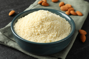 Fresh almond flour in bowl on dark textured table, closeup
