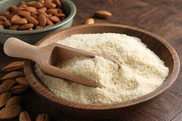 Fresh almond flour, scoop in bowl and nuts on wooden table, closeup