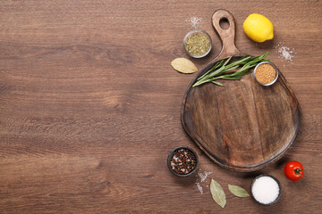 Cutting board, spices, lemon and tomato on wooden table, flat lay. Space for text