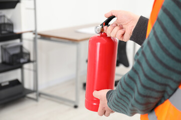 Man with fire extinguisher indoors, closeup. Space for text
