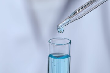 Dripping liquid from pipette into test tube on blurred background, closeup