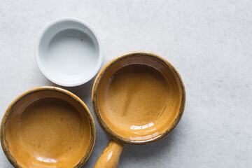 Top view of brown and white ceramic ramekins on a white marble countertop, terracotta ramekins with handles on a white background