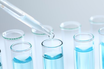 Dripping liquid from pipette into test tube on light background, closeup